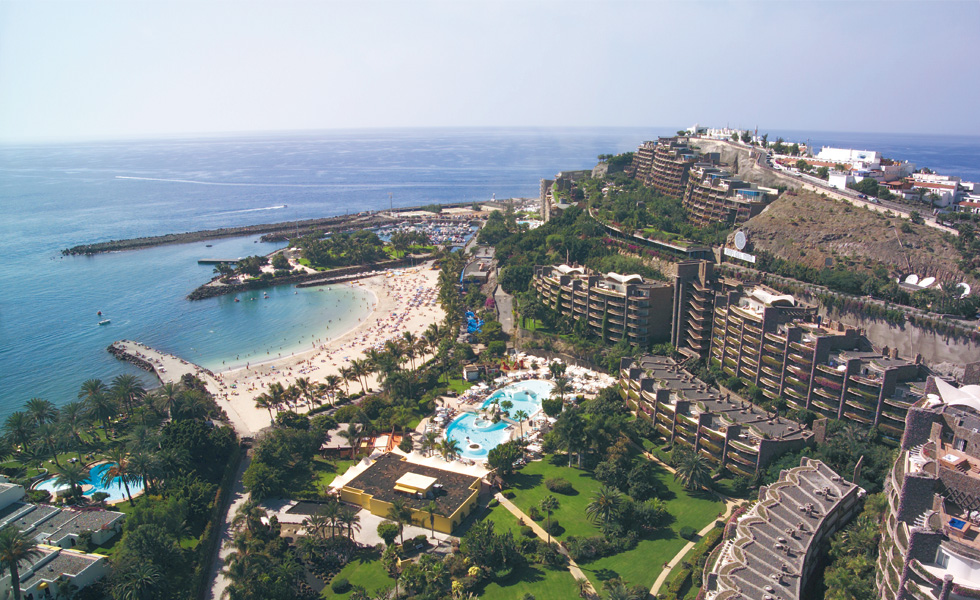 Aerial view of a sunlit Costa del Sol resort crescent with beach, pools and marina